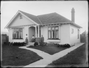 Exterior view of a single-storey wooden bungalow, with two women and a man, all unidentified, possibly Christchurch district