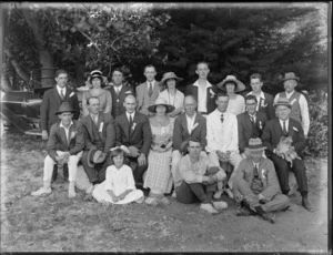 Group of unidentified men, women and girl, one man holds a small dog, and there is a motorcar behind, in an outdoor location, possibly Christchurch district