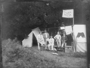 Group of five unidentified men, some wearing top hats, standing next to two tents, one of which has a flag reading 'Flax Camp', at a campsite, possibly Christchurch district
