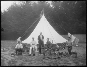 Five unidentified men, at a campsite, performing domestic tasks, including chopping wood, polishing shoes, and peeling vegetables, possibly Christchurch district