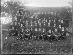 A group of unidentified men, in front of a delapidated house, possibly Christchurch district