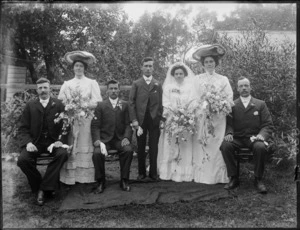 Wedding portrait of unidentified bride and groom with wedding party, taken in the garden, possibly Christchurch district