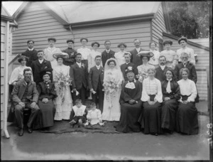 Wedding portrait of unidentified bride and groom with wedding party and family members, at the back of the house, possibly Christchurch district