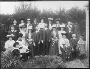 Wedding portrait of unidentified bride and groom with wedding party and family members, in the garden at the back of the house, possibly Christchurch district