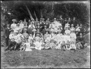 A group of unidentified men, women and children, in an unidentified park under a row of trees, possibly Christchurch district