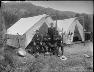 Four unidentified men, three sitting and one standing in front of a tent, showing a washing basin, pots and a teapot with cups of tea, camping ground unidentified, possibly Christchurch district
