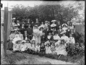 A wedding portrait of an unidentified bride and groom with the wedding party and family members, in the garden at the back of the house, probably Christchurch district