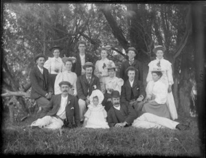 A group of unidentified people, six men, six women and a child under a row of trees in an unidentified park, possibly Christchurch district