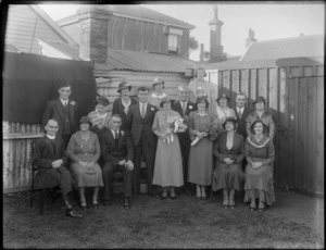 Wedding portrait of unidentified bride and groom with wedding party and family members and the clergyman in the backyard, probably Christchurch district, showing houses in the background