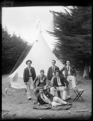Six unidentified men at the campsite, possibly Christchurch district, showing a man lying on a blanket in the front, with two men sitting on stools and three men standing behind them in front of the tent