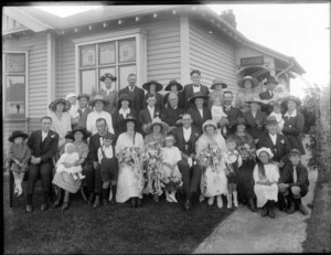 Wedding portrait of a unidentified bride and groom with the wedding party and family members in the garden in front of the house, possibly Christchurch district, showing a sign Te Mahu above the archway to the front door of the house