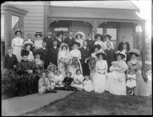 Wedding portrait of unidentified bride and groom with the wedding party and family members, in front of a house, possibly Christchurch district
