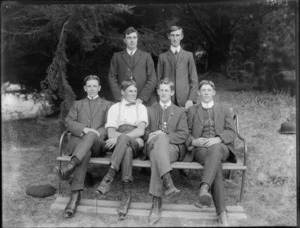 Six unidentified men, showing four men sitting on a wooden bench and two men standing behind them, in an unidentified park, possibly Christchurch district