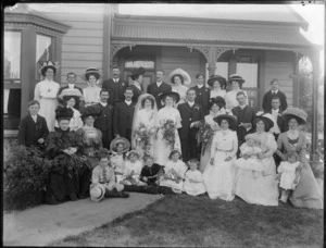 Wedding portrait of unidentified bride and groom with wedding party and family members, in front of a house, possibly Christchurch district