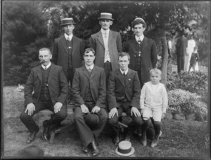 A group of six unidentified men and a boy, showing three men and the boy sitting on a wooden bench with three men standing behind them, in a park, possibly Christchurch district