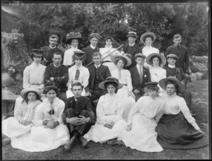 A group of unidentified people, men and women, showing some of the men wearing a brass band uniform, a women in the back row holding a slide trombone, in an unidentified park, possibly Christchurch district