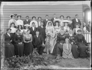 Wedding portrait of a unidentified bride and groom with wedding party and family members, in the garden beside a house, possibly Christchurch district