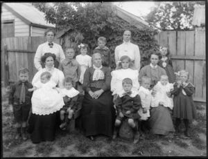 Unidentified family group portrait, showing five women, six boys, four girls and two babies, in a backyard, possibly Christchurch district