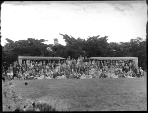 A group of unidentified people, showing men, women and children sitting and standing in front of two tents, in an unidentified park, possibly Christchurch district