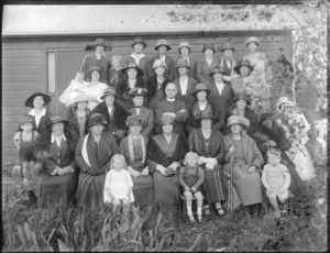 A group of unidentified women, children and a clergyman sitting and standing beside an unidentified building, possibly Christchurch district
