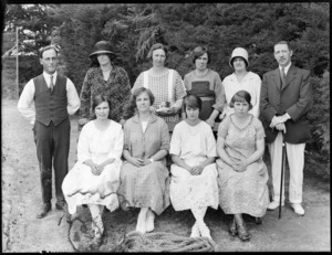 A group of unidentified people, eight women and two men, showing four women sitting on a wooden bench, four standing behind them and the two men standing on either side of the women on the bench, in an unidentified park, possibly Christchurch district