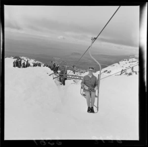 An unidentified woman on a chairlift at the New Zealand Ski Championship at Mt Ruapehu, showing skiers and spectators in the background