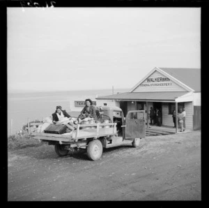 Two women sitting on the back of a utility vehicle outside Walker Bros general store, Te Kaha