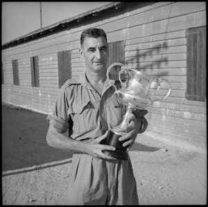 Sgt Mjr C G Fearon, Captain of the NZ Forces Rowing Club, holding cup, Cairo