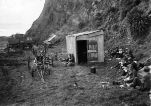 A group of men, sitting around a hut, Lyall Bay