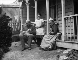 Three people and two dogs by the verandah of a house
