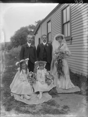 Wedding portrait of unidentified bride and groom, with the best man and the flowergirls, in the garden beside a house, possibly Christchurch district