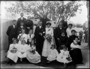 Unidentified wedding group outdoors under a tree, probably Christchurch district, showing bride and groom, wedding party and extended families