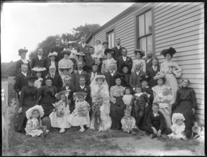 Wedding portrait of unidentified bride and groom with wedding party and family members, in the garden beside a house, possibly Christchurch district