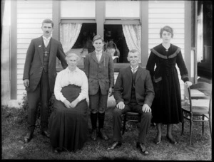 Unidentified family group outside house, probably Christchurch district, including a view of the parlour through the windows behind