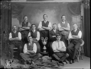 Studio portrait of unidentified men, possibly a tug of war team, with trophy, probably Christchurch district, includes rope in front