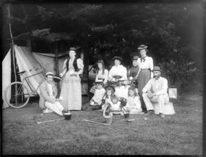 Group of unidentified men, women and girls outside a tent, possibly Sumner, Christchurch, includes a bicycle to the left