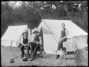 Group of unidentified male youths at a campsite, one youth holding a piano accordian, flag sign on tents reads 'Clover', probably Christchurch district