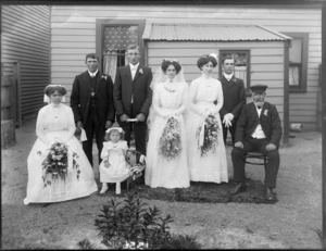 Unidentified wedding group outside house, showing bride and groom, groomsmen, bridesmaids, flowergirl and [father of bride?], probably Christchurch district