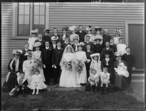 Unidentified Wedding party portrait on grass outdoors, with bride in veil, groom, extended family, children, women in hats, probably Christchurch region