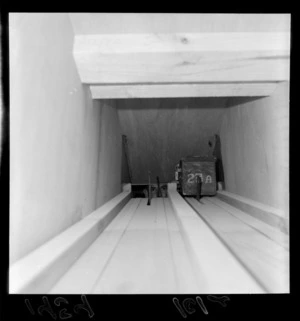 Man looking down a shaft at a cashbox as it is returned after a bus driving shift, Lower Hutt Bus Terminal