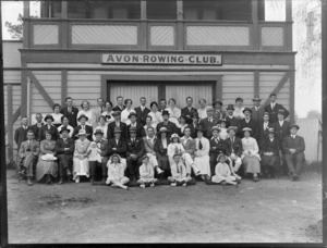 Large group portrait of unidentified adults with hats and children with caps in front of the Avon Rowing Club building with balcony, Christchurch