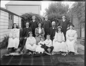 Unidentified family portrait in back yard by wooden building and fence, probably Christchurch region