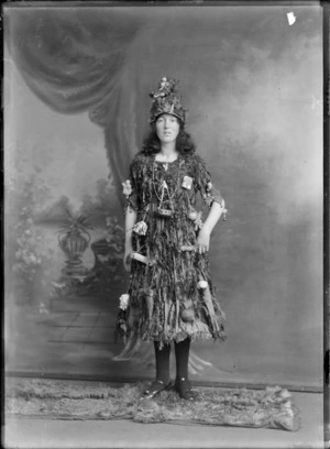Studio portrait of unidentified young woman in Christmas tree fancy dress and hat costume, with little presents and decorations hanging off her, Christchurch
