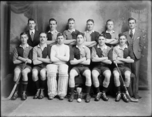 Studio portrait of unidentified men's hockey team in uniforms and coaches, with pads, hockey sticks, cup and ball in front, Christchurch