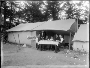 Four unidentified men and two boys having tea at a table under an awning between two tents with 'Raukura' camp sign, tall trees beyond, [Sumner?], Christchurch