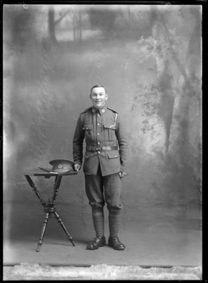 Studio portrait of unidentified soldier in uniform, with hat and swagger stick on table, probably Christchurch district