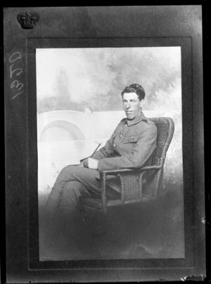 Studio portrait of an unidentified man wearing a military uniform, sitting in a wicker chair