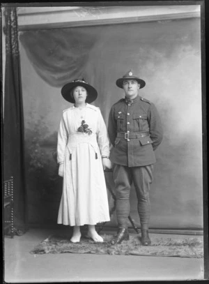 Studio portrait of an unidentified man and woman, the man wears a military uniform, and the woman has a corsage at her waist, possibly Christchurch