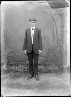 Portrait of an unidentified man, outdoors, with a painted studio backdrop, possibly Christchurch