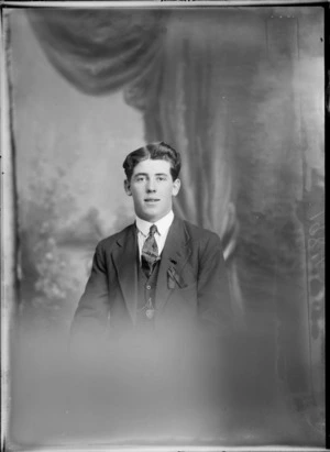 Studio portrait of an unidentified young man with an unusual pin and a ribbon attached to lapel, possibly Christchurch